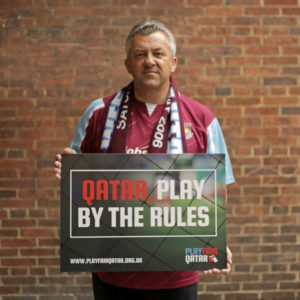 A fan in West Ham kit holds a Playfair Qatar sign